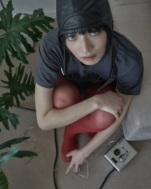 レザーのパイロットキャップと赤いタイツを着用ししゃがみ込む小松菜奈さん