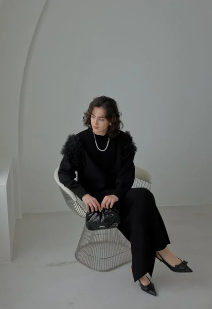 黒い服とパールネックレスを身につけた人物がモダンな椅子に座る