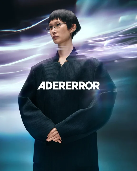 短い髪と眼鏡をかけた女性がオーバーサイズのダークスーツを着用している画像