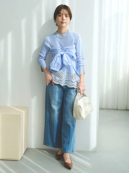 水色のニットとストライプシャツをレイヤードし、ワイドデニムパンツを合わせた女性