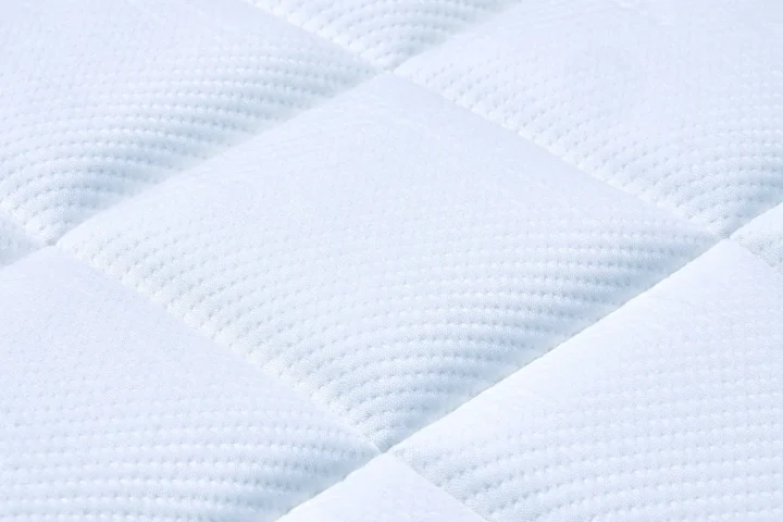白いキルティング加工された生地のクローズアップです。柔らかく、快適そうな質感で、マットレスや寝具の表面を思わせます。清潔感があり、シンプルで落ち着いた印象を与えます。