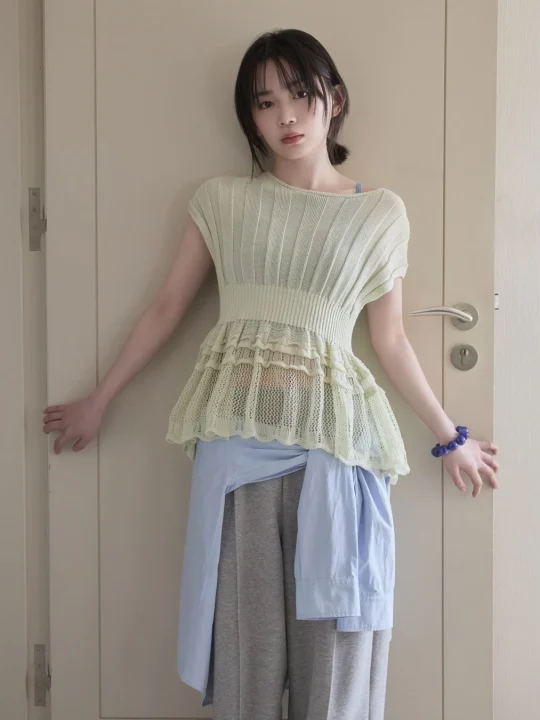 淡い緑色のニットトップスとグレーのワイドパンツを着用した若い女性