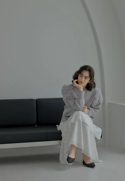グレーのふわふわ袖トップスと白いロングスカートを着た女性