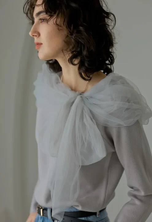 グレーのニットに同色のチュールをあしらったトップスを着た女性