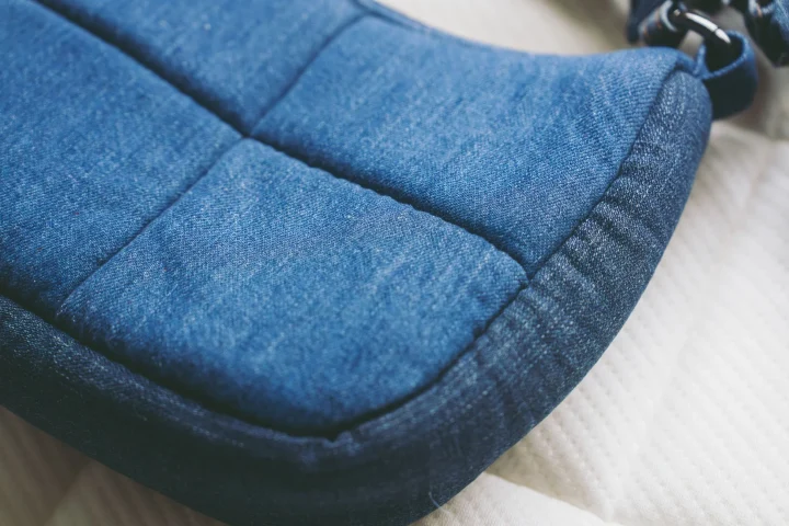 青いデニム生地のようなキルティング素材のアイテムが、白い布地の上に置かれているクローズアップ写真です。カジュアルで温かみのある質感が特徴です。