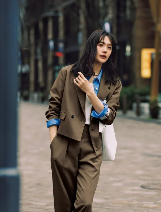 茶色のスーツと青いシャツを着用した女性が街中を歩く様子