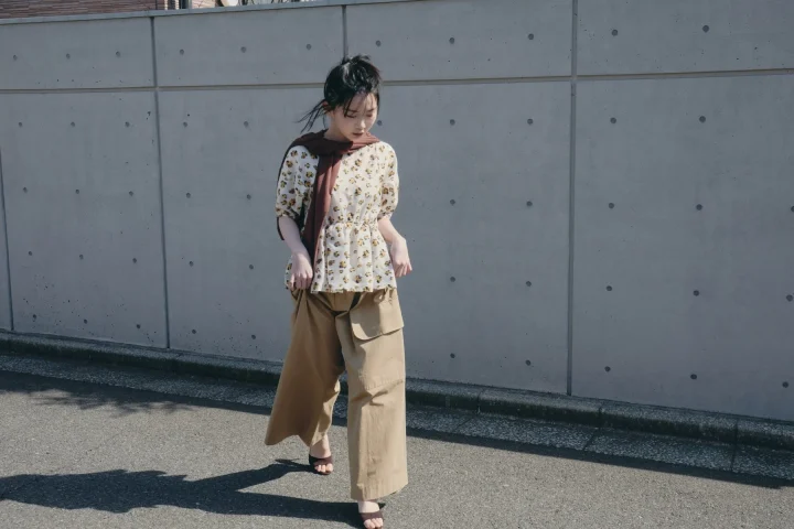 花柄のトップスにベージュのワイドカーゴパンツを合わせ、ブラウンのスカーフを肩にかけた女性