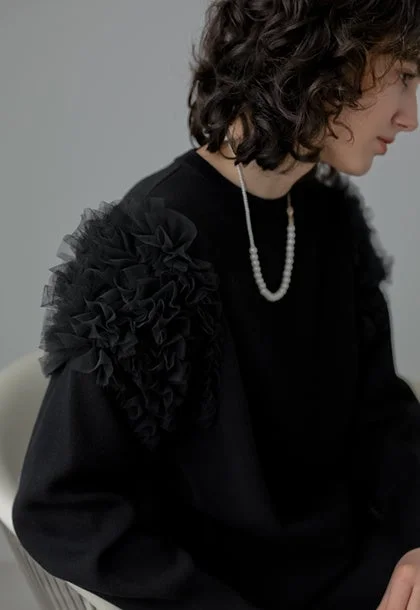 黒いフリル付きトップスとパールネックレスをつけた女性のポートレート