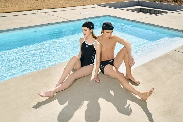 水着とスイミングキャップを着用した男女がプールサイドに座っている様子