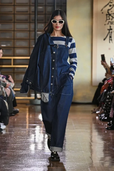 ボーダーシャツの上にデニムのオーバーオールとジャケットを合わせたカジュアルな装いの女性モデル。