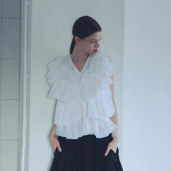白いフリルブラウスと黒いパンツを着用した女性
