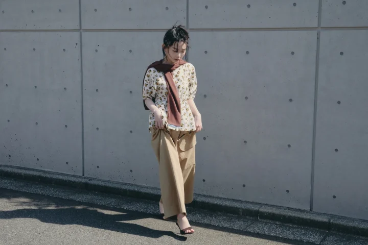 花柄ブラウスとベージュのワイドパンツに、ブラウンのカーディガンを肩掛けした女性