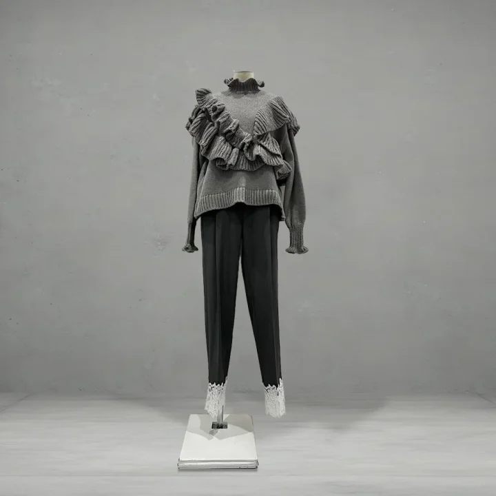 グレーのフリル付きセーターと、裾に白いレースがあしらわれたダークカラーのパンツ