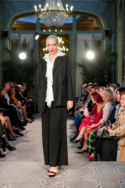 黒いスーツと白いフリルブラウスを着用したモデル