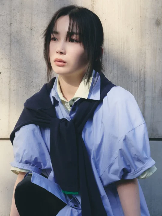 青いシャツにネイビーのセーターを肩掛けした若い女性