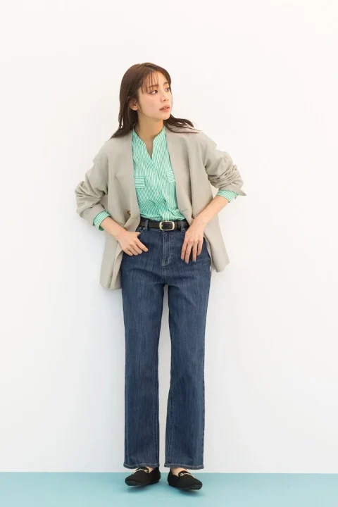 ベージュのジャケットとグリーンのストライプシャツ、濃い青のデニムを着用した女性の全身コーディネート。黒いベルトとローファーを合わせ、きれいめカジュアルな着こなしです。