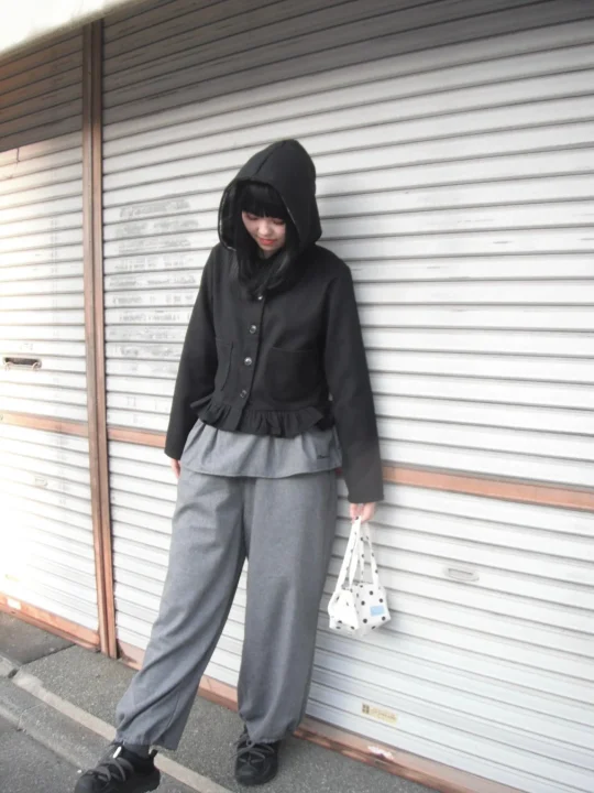 黒いフード付きジャケットとグレーのワイドパンツを着用した女性