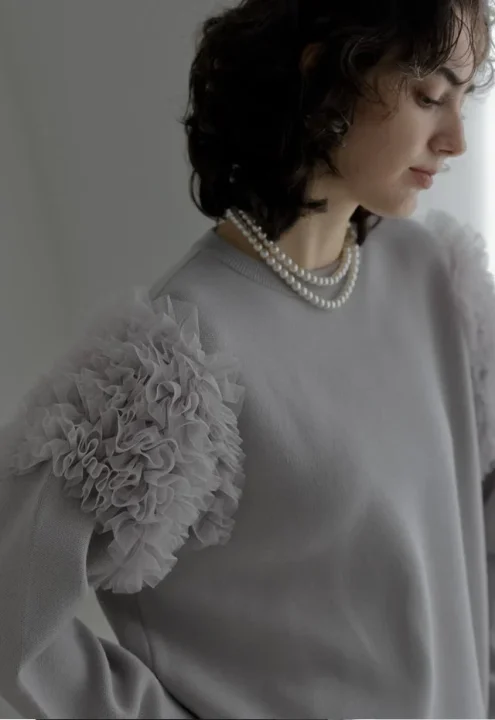 フリル袖のグレーセーターとパールネックレスを着用した女性