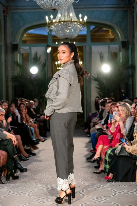 グレーのフリル付きセーターと裾に白いレースがあしらわれたパンツを着用したモデル