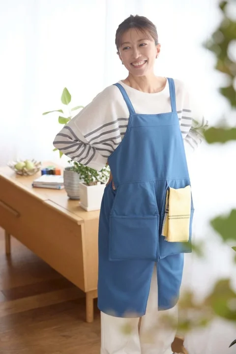 ライトブルーのエプロンを着用し、笑顔で立つ女性