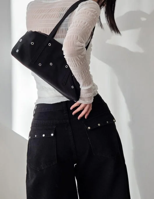 白いシアーなトップスと黒いワイドパンツを着用した女性の後ろ姿。スタッズ付きカーゴポケットとアイレットが特徴の黒いショルダーバッグがアクセントの、カジュアルで洗練されたモノトーンコーディネートです。