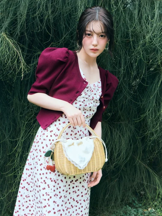 チェリー柄のワンピースとボルドーのカーディガンを着用した若い女性
