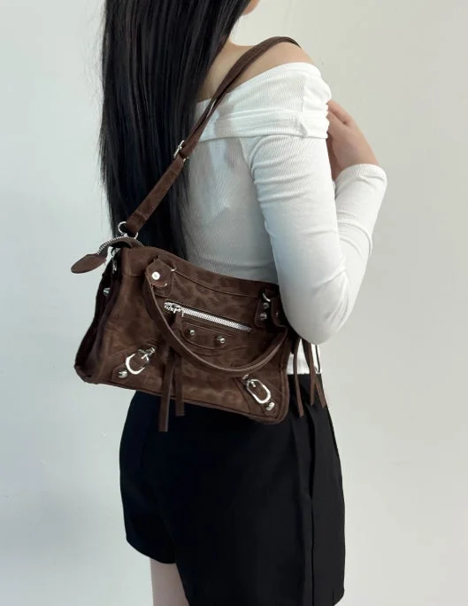 白いオフショルダートップスと黒のショートパンツを着用し、茶色のスエード調ショルダーバッグを肩にかけた女性の後ろ姿。カジュアルながらも洗練されたファッションスタイルが特徴的です。