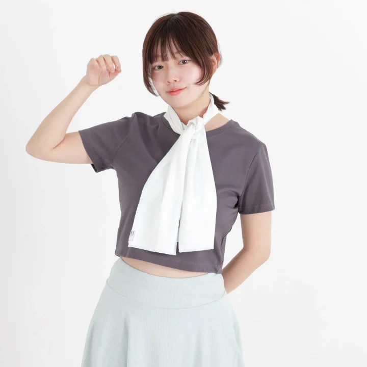 グレーのクロップトップと水色のスカートを着用し、白いスカーフを首に巻いています。