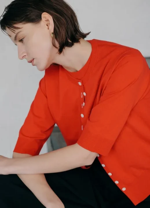 明るい赤の半袖カーディガンを着用した女性の横顔のクローズアップ。