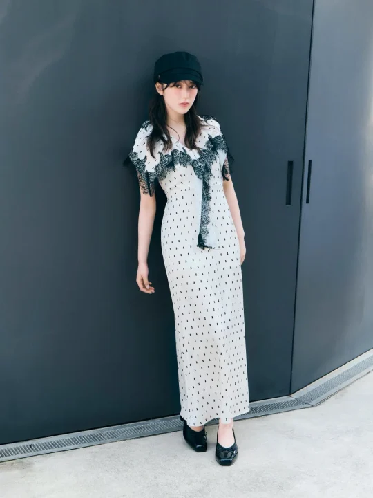 白いロングワンピースに黒い模様とレースがあしらわれ、黒いキャスケットと靴を合わせたシックなファッションの女性