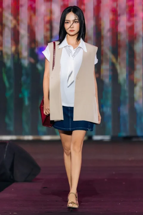 白いブラウスにベージュのベスト、デニムのミニスカートを着用したモデル