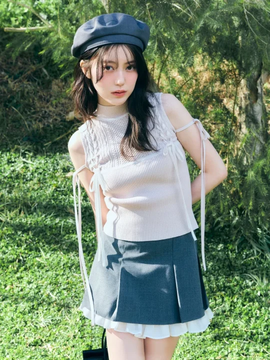 緑豊かな屋外で、ベレー帽とリボン付きのノースリーブトップス、プリーツスカートを着用した若い女性