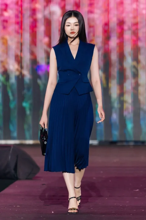 ネイビーのノースリーブトップスとプリーツスカートのエレガントなセットアップを着用したモデル