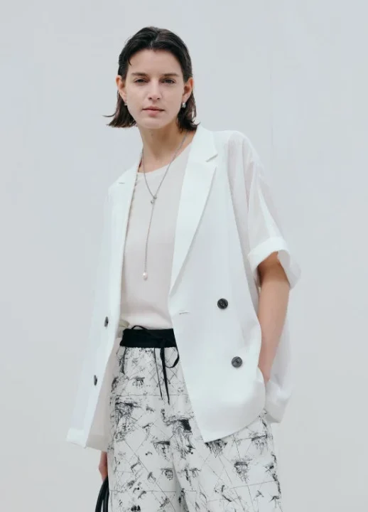 白い半袖ジャケットと柄物のパンツを着用した女性。クリーンでスタイリッシュな夏の装い。
