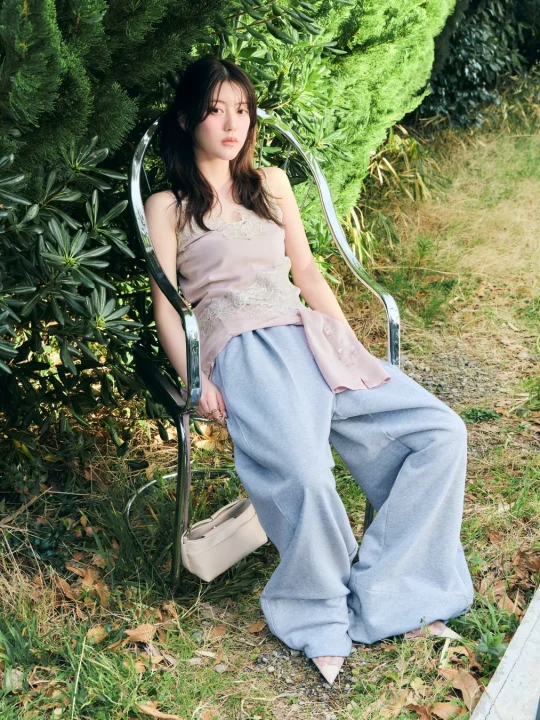 緑豊かな屋外で、若い女性が金属製の椅子に座ってポーズをとっています