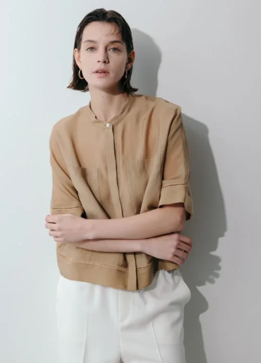 ベージュのスタンドカラーブラウスと白いパンツを着用した女性のポートレート。