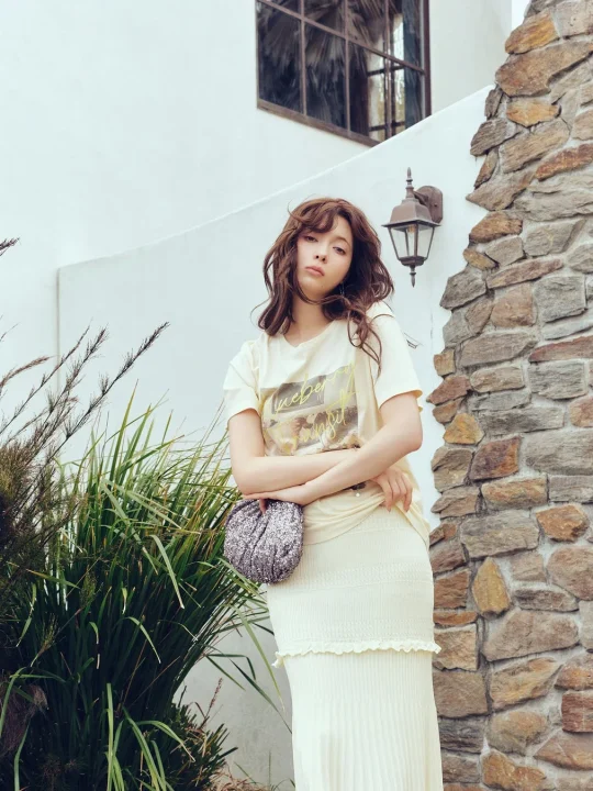 クリーム色のTシャツとロングスカート、キラキラバッグの屋外ショット