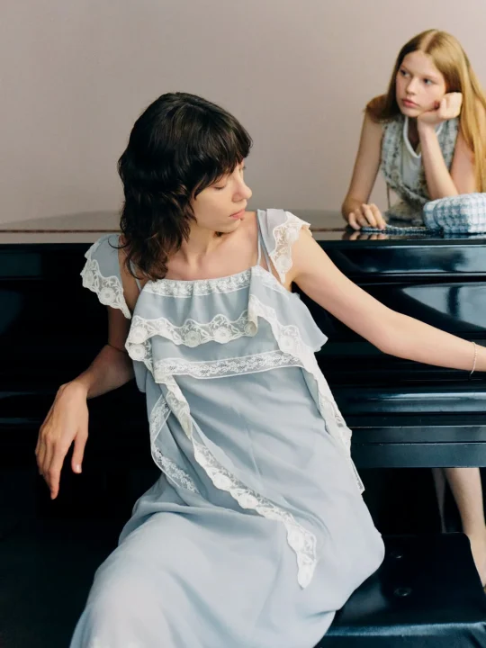 水色のレースドレスを着た女性がピアノの前に座る