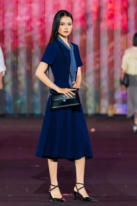 ネイビーのドレスと黒いハンドバッグ、ハイヒールを身につけたモデル