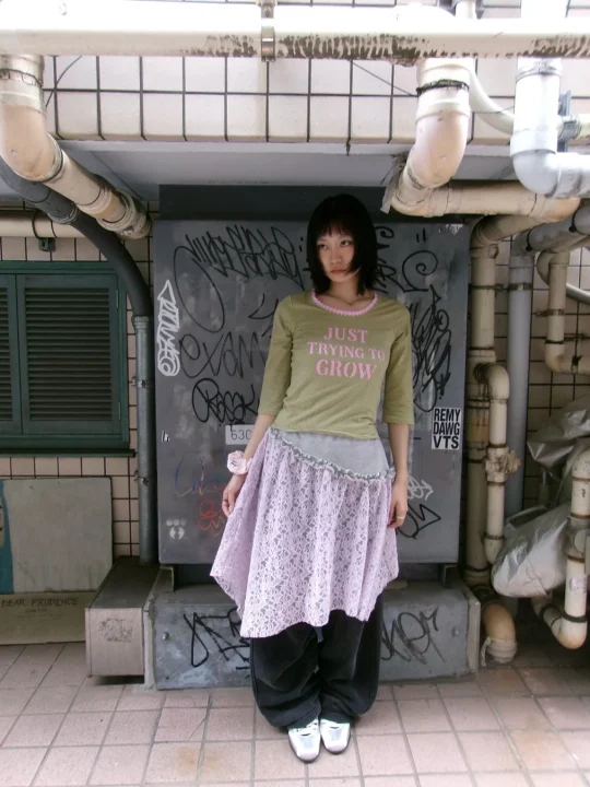 女性、ファッション、ストリートスタイル、レイヤード、レーススカート、グラフィックTシャツ、ゆるいパンツ、スニーカー、ボブヘア、都会、グラフィティ、パイプ、コンクリート、カジュアル、個性的なファッション