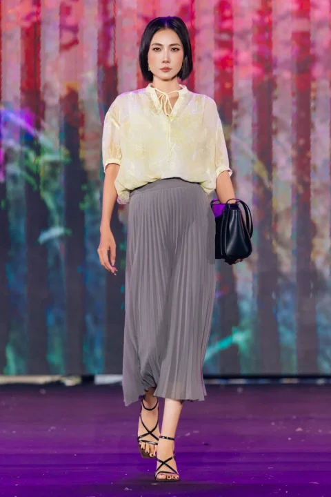 淡い黄色のシアーなブラウスとグレーのプリーツスカートを組み合わせたモデル