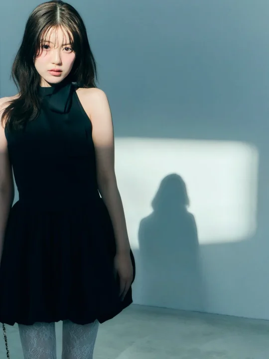 黒いハルターネックのミニドレスと白いレースタイツを着用した若い女性