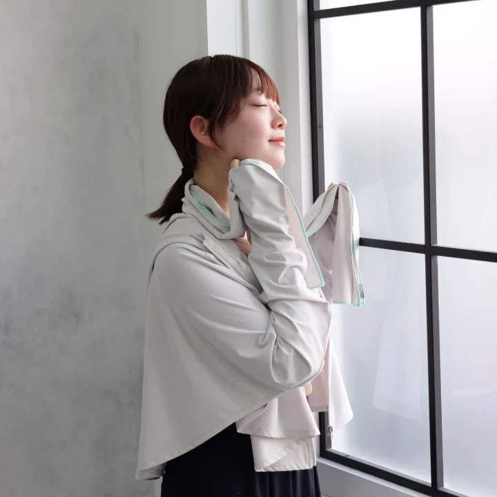 女性が窓辺で目を閉じ、リラックスした表情でタオルを手に持っています。