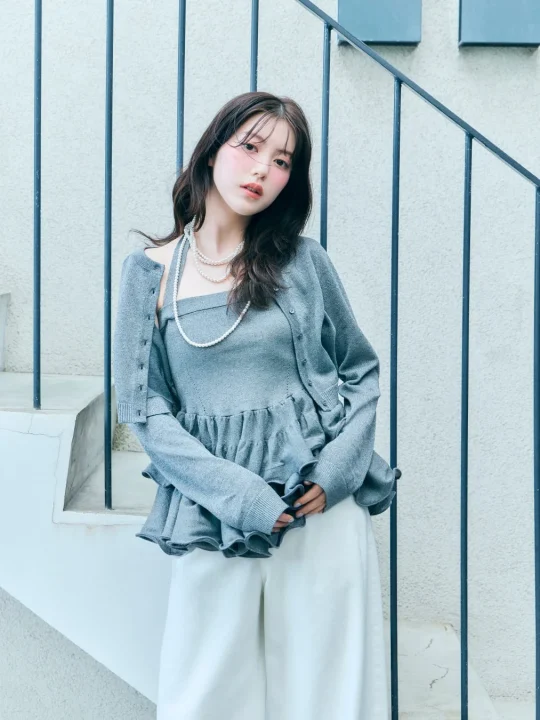 グレーのニットアンサンブルと白いワイドパンツを着た若い女性