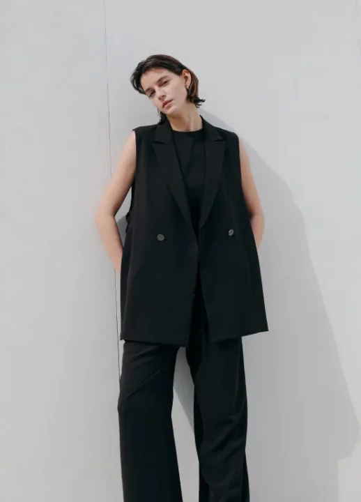 黒いノースリーブのロングベストとワイドパンツを着用した女性。クールでミニマルなファッションスタイル。