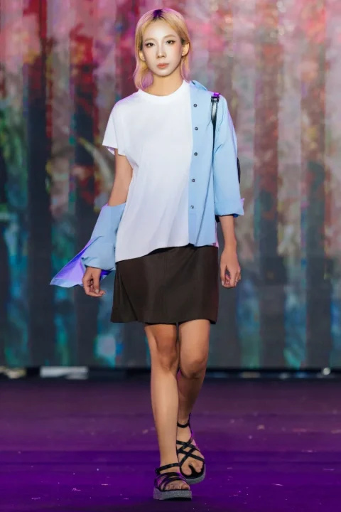 白いTシャツと水色のシャツ、茶色のミニスカートを着用しランウェイを歩くモデル