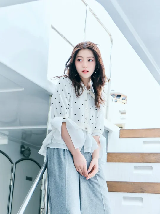 白いドット柄のシャツとグレーのパンツを着た若い女性がヨットの階段に立つポートレート