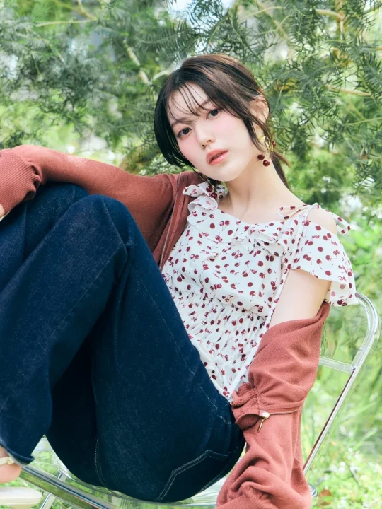 チェリー柄のトップスにデニムとカーディガンを合わせたカジュアルな装いの女性