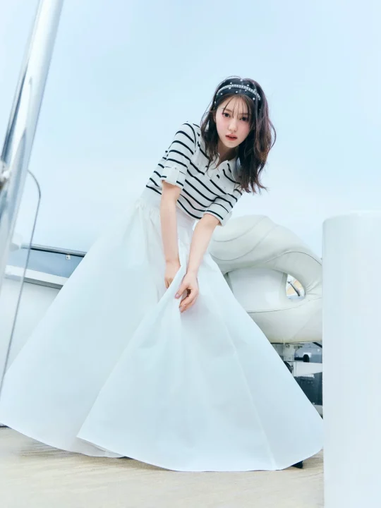 ヨットの上で、ストライプのトップスと白いロングスカートを着用し、カチューシャをつけた若い女性