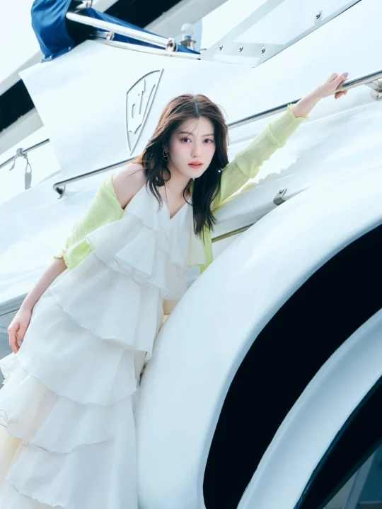 白いティアードドレスにライムグリーンのカーディガンを羽織り、優雅な表情でカメラを見つめる女性